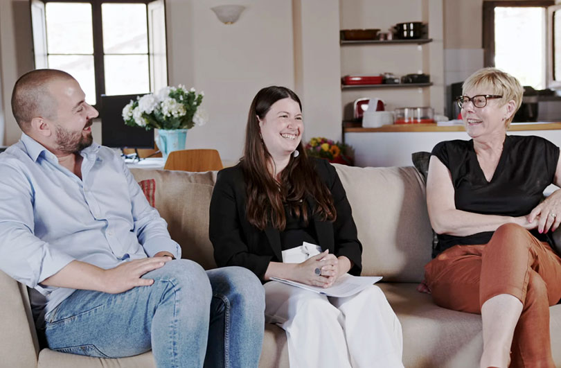 Tre persone sedute su un divano che conversano in un moderno soggiorno.