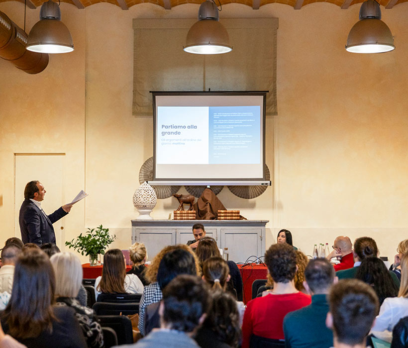 Presentazione aziendale in sala conferenze con pubblico e schermo di proiezione.