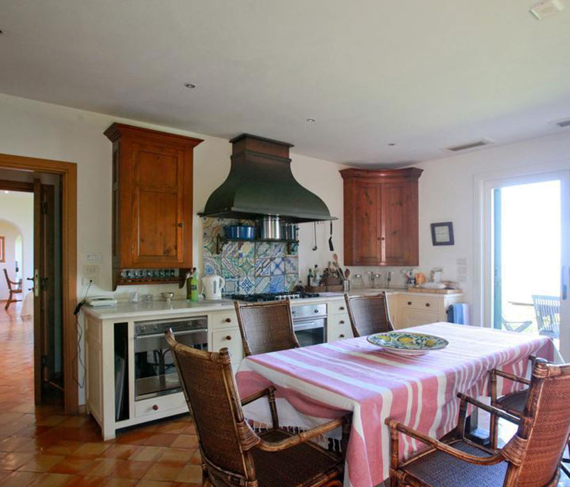 Cucina tradizionale con mobili in legno, grande cappa, piastrelle colorate e tavolo da pranzo con sedie in vimini.