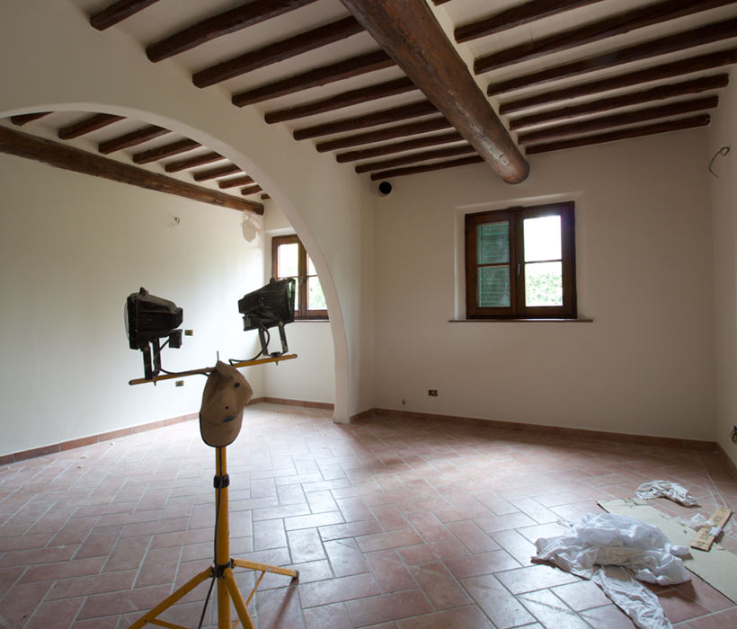 Ampia stanza con pavimento in cotto, soffitto con travi in legno, arco e finestra luminosa.