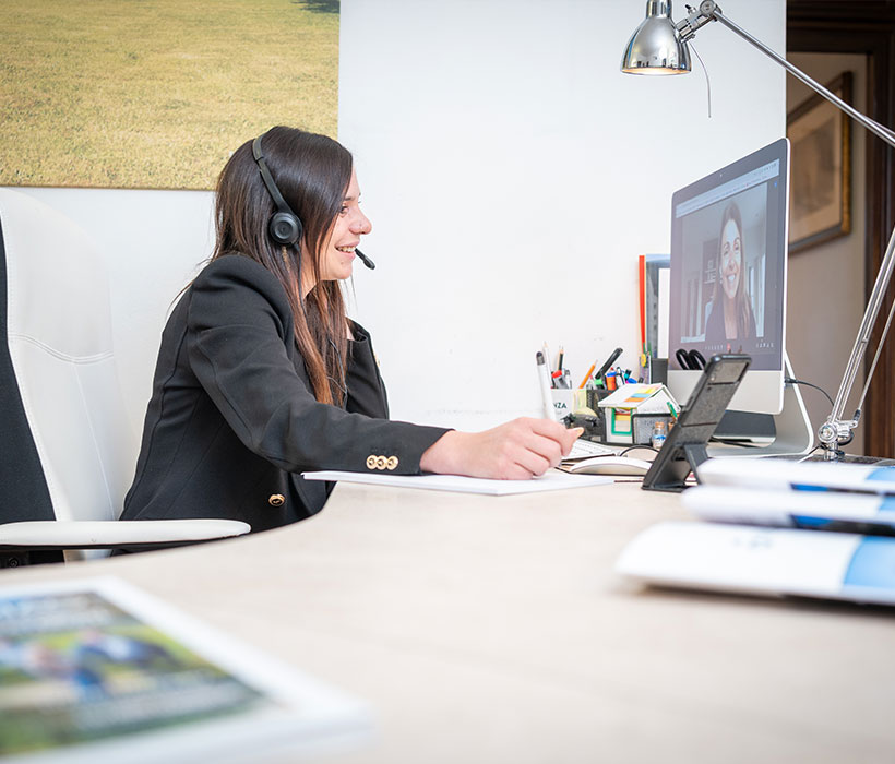 Donna con cuffie al computer durante una videochiamata in ufficio moderno con documenti.
