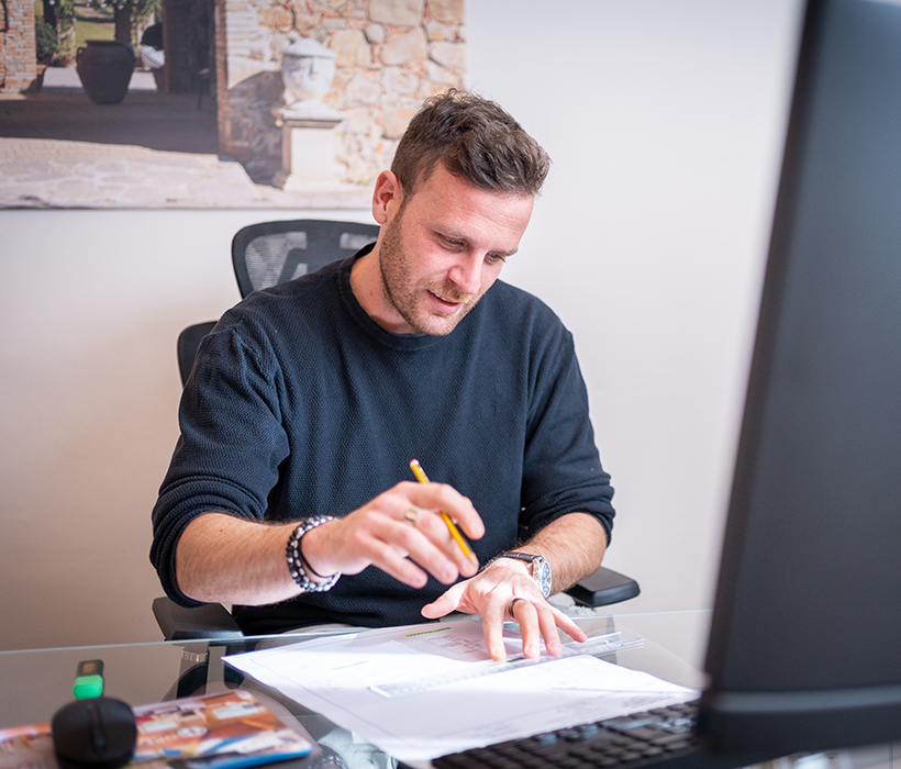 Uomo che lavora alla scrivania con documenti e computer in un ufficio moderno.