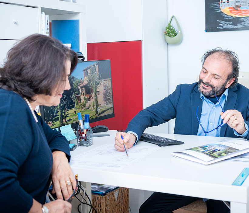 Agente immobiliare discute documenti immobiliari con una cliente in un ufficio moderno.
