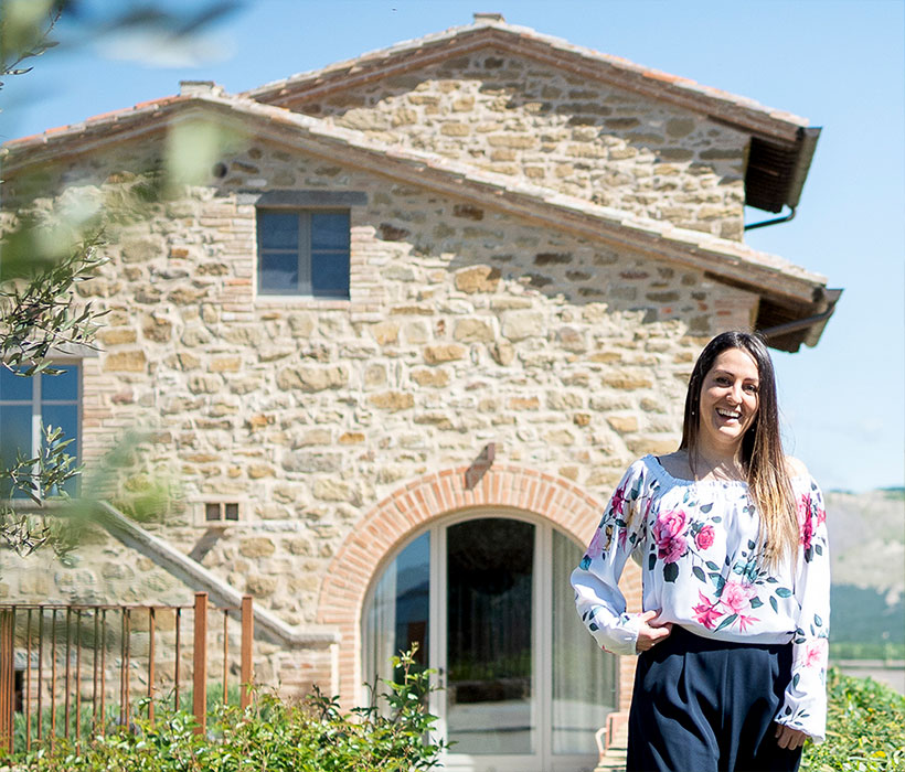Casa in pietra con porta ad arco e donna sorridente in giardino.