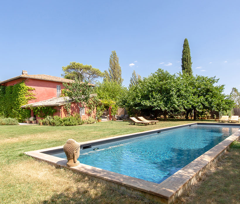 Affascinante villa con pareti rosse, giardino e grande piscina rettangolare con lettini.