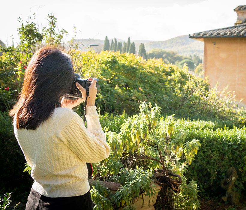 Donna fotografa giardino rigoglioso e vista campagna vicino a casa rustica.
