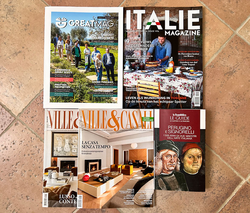 Quattro riviste disposte su un pavimento piastrellato, dedicate a lifestyle, propriet\u00e0 e arte.